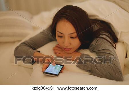 Stock Image - Young attractive Japanese woman with smartphone in bed. Fotosearch