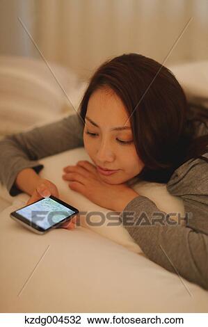 Stock Image - Young attractive Japanese woman with smartphone in bed. Fotosearch