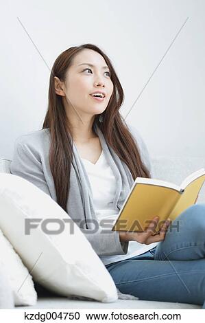 Stock Image - Young attractive Japanese woman with book on the sofa. Fotosearch