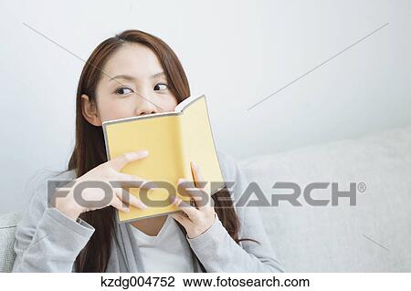 Stock Image - Young attractive Japanese woman with book on the sofa. Fotosearch