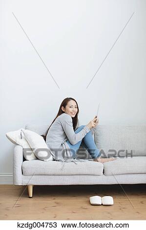 Stock Image - Young attractive Japanese woman with tablet on the sofa. Fotosearch