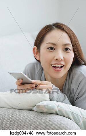 Young attractive Japanese woman with smartphone on the sofa View Large Photo Image Stock Photo - Young attractive Japanese woman with smartphone on the sofa. Fotosearch