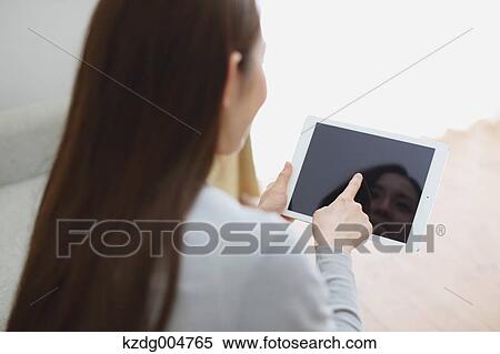 Stock Photography - Young attractive Japanese woman with tablet on the sofa. Fotosearch