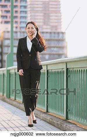 Stock Image - Young Japanese businesswoman on the phone by a river downtown Tokyo. Fotosearch