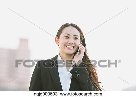 Stock Image - Young Japanese businesswoman on the phone by a river downtown Tokyo. Fotosearch