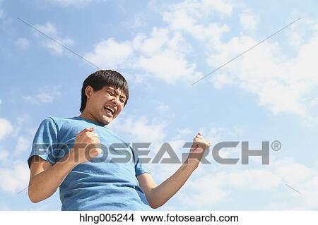 Young Japanese man cheering against blue sky View Large Photo Image Picture - Young Japanese man cheering against blue sky. Fotosearch