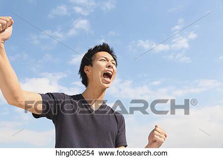 Young Japanese man cheering against blue sky View Large Photo Image Picture - Young Japanese man cheering against blue sky. Fotosearch