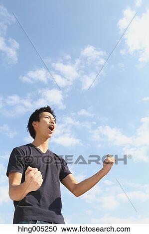 Young Japanese man cheering against blue sky View Large Photo Image Stock Image - Young Japanese man cheering against blue sky. Fotosearch