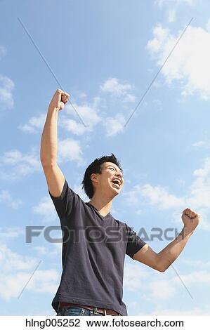 Young Japanese man cheering against blue sky View Large Photo Image Stock Image - Young Japanese man cheering against blue sky. Fotosearch