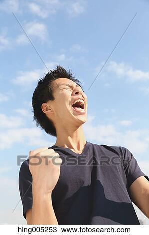 Young Japanese man cheering against blue sky View Large Photo Image Stock Image - Young Japanese man cheering against blue sky. Fotosearch