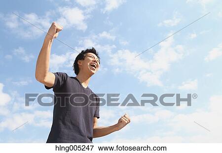 Young Japanese man cheering against blue sky View Large Photo Image Stock Photo - Young Japanese man cheering against blue sky. Fotosearch