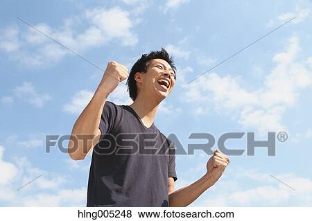 Young Japanese man cheering against blue sky View Large Photo Image Stock Photo - Young Japanese man cheering against blue sky. Fotosearch