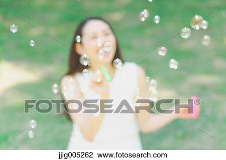 Young Japanese woman blowing soap bubbles in a city park View Large Photo Image Stock Image - Young Japanese woman blowing soap bubbles in a city park. Fotosearch
