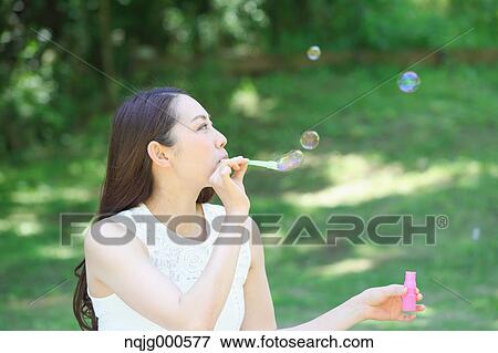Stock Photo - Young Japanese woman blowing soap bubbles in a city park. Fotosearch