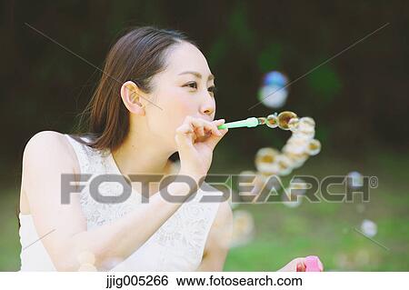 Stock Photograph - Young Japanese woman blowing soap bubbles in a city park. Fotosearch