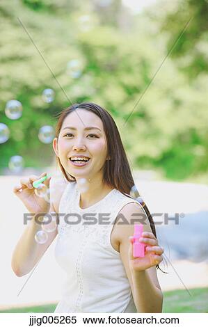Stock Photography - Young Japanese woman blowing soap bubbles in a city park. Fotosearch