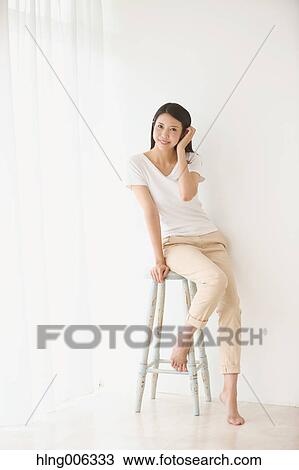 Stock Image - Young Japanese woman on a chair in a white room. Fotosearch