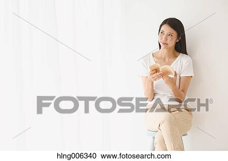 Stock Image - Young Japanese woman on a chair in a white room. Fotosearch