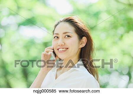 Young Japanese woman on the phone surrounded by green in a city park View Large Photo Image Stock Photography - Young Japanese woman on the phone surrounded by green in a city park. Fotosearch
