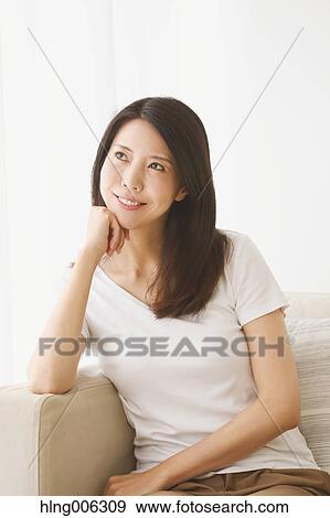 Stock Photo - Young Japanese woman on the sofa in a white room. Fotosearch
