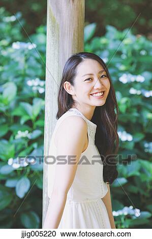 Stock Image - Young Japanese woman on wooden deck in a city park. Fotosearch