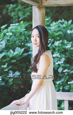 Stock Image - Young Japanese woman on wooden deck in a city park. Fotosearch