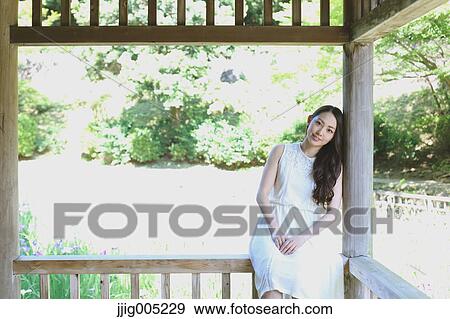 Stock Photo - Young Japanese woman on wooden deck in a city park. Fotosearch