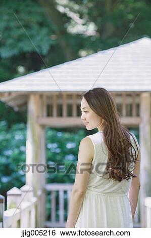 Stock Photograph - Young Japanese woman on wooden deck in a city park. Fotosearch
