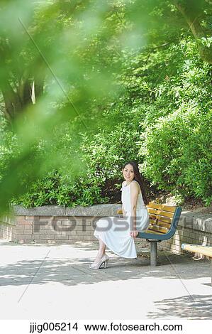 Young Japanese woman sitting on a bench in a city park View Large Photo Image Picture - Young Japanese woman sitting on a bench in a city park. Fotosearch