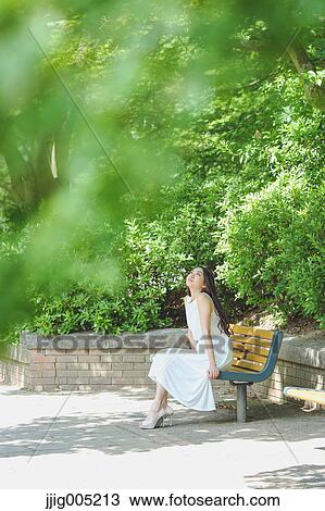 Young Japanese woman sitting on a bench in a city park View Large Photo Image Stock Image - Young Japanese woman sitting on a bench in a city park. Fotosearch