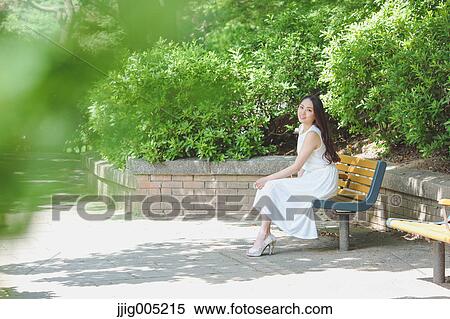 Stock Photography - Young Japanese woman sitting on a bench in a city park. Fotosearch