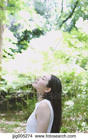 Picture - Young Japanese woman surrounded by green in a city park. Fotosearch