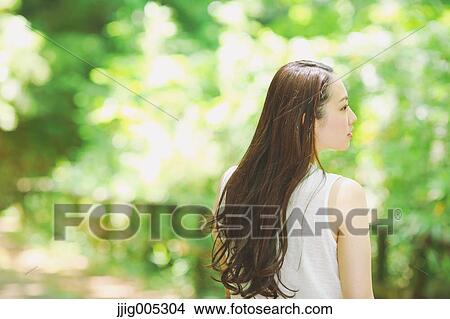 Picture - Young Japanese woman surrounded by green in a city park. Fotosearch