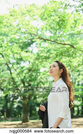 Young Japanese woman surrounded by green in a city park View Large Photo Image Picture - Young Japanese woman surrounded by green in a city park. Fotosearch