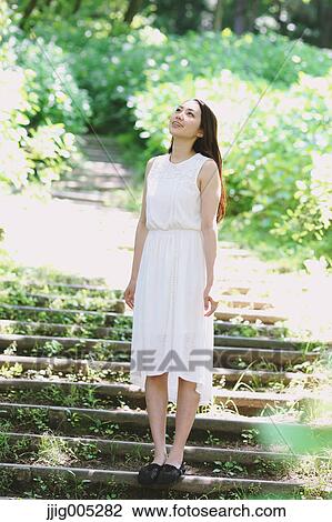 Stock Image - Young Japanese woman surrounded by green in a city park. Fotosearch