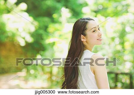 Stock Image - Young Japanese woman surrounded by green in a city park. Fotosearch