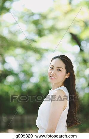 Stock Image - Young Japanese woman surrounded by green in a city park. Fotosearch