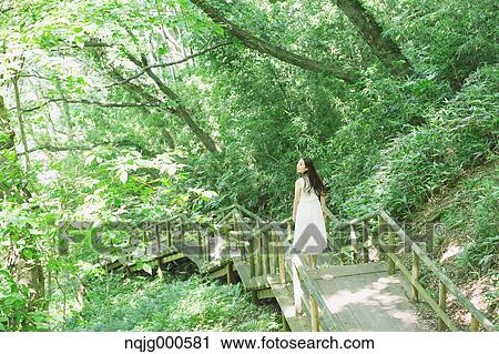 Stock Image - Young Japanese woman surrounded by green in a city park. Fotosearch