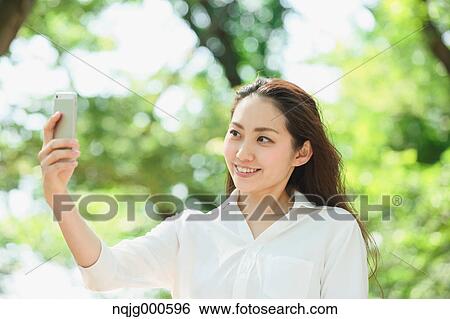 Young Japanese woman taking selfie surrounded by green in a city park View Large Photo Image Stock Photograph - Young Japanese woman taking selfie surrounded by green in a city park. Fotosearch