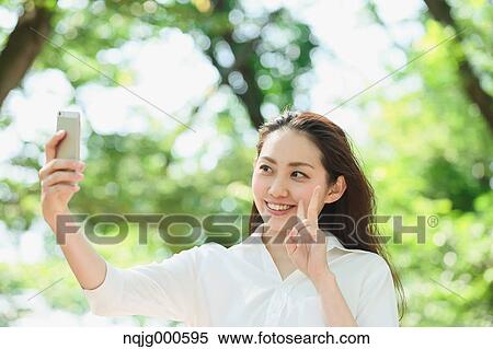 Young Japanese woman taking selfie surrounded by green in a city park View Large Photo Image Stock Photography - Young Japanese woman taking selfie surrounded by green in a city park. Fotosearch