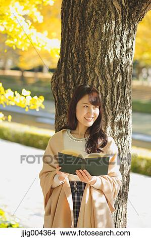 Picture - Young Japanese woman with book in a city park. Fotosearch
