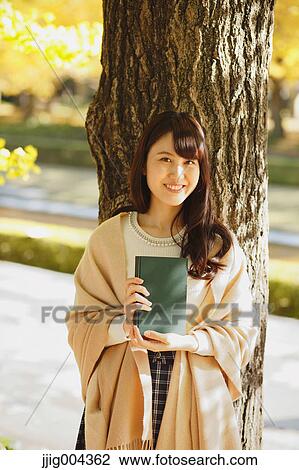 Young Japanese woman with book in a city park View Large Photo Image Stock Image - Young Japanese woman with book in a city park. Fotosearch
