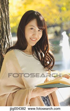 Stock Image - Young Japanese woman with book in a city park. Fotosearch