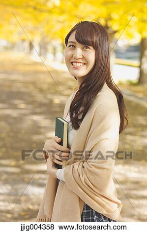 Stock Photo - Young Japanese woman with book in a city park. Fotosearch