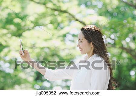 Young Japanese woman with smartphone surrounded by green in a city park View Large Photo Image Stock Image - Young Japanese woman with smartphone surrounded by green in a city park. Fotosearch