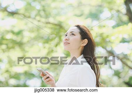 Young Japanese woman with smartphone surrounded by green in a city park View Large Photo Image Stock Photo - Young Japanese woman with smartphone surrounded by green in a city park. Fotosearch