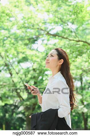 Young Japanese woman with smartphone surrounded by green in a city park View Large Photo Image Stock Photo - Young Japanese woman with smartphone surrounded by green in a city park. Fotosearch