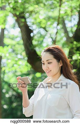 Young Japanese woman with smartphone surrounded by green in a city park View Large Photo Image Stock Photo - Young Japanese woman with smartphone surrounded by green in a city park. Fotosearch