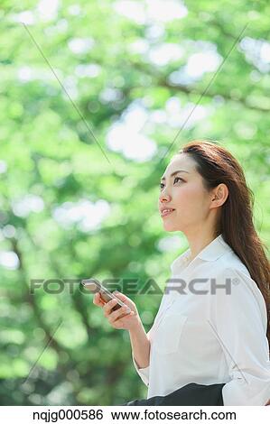 Young Japanese woman with smartphone surrounded by green in a city park View Large Photo Image Stock Photograph - Young Japanese woman with smartphone surrounded by green in a city park. Fotosearch