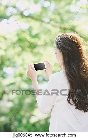 Young Japanese woman with smartphone surrounded by green in a city park View Large Photo Image Stock Photography - Young Japanese woman with smartphone surrounded by green in a city park. Fotosearch
